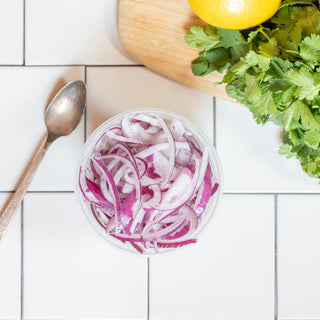 Sliced Red Onion in a reusable container on tile background