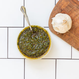 Castelvetrano Olive Chimichurri in a reusable container with a cutting board