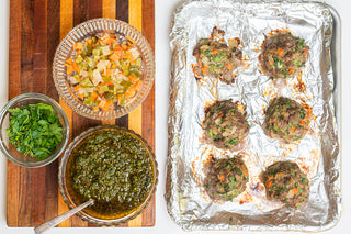 meatballs on a pan covered with tinfoil next to a bowl of chimichurri